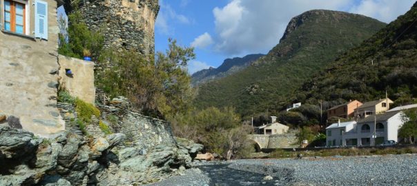 Historic stone buildings and lush mountains in Olmeta-di-Capocorso, Corsica.