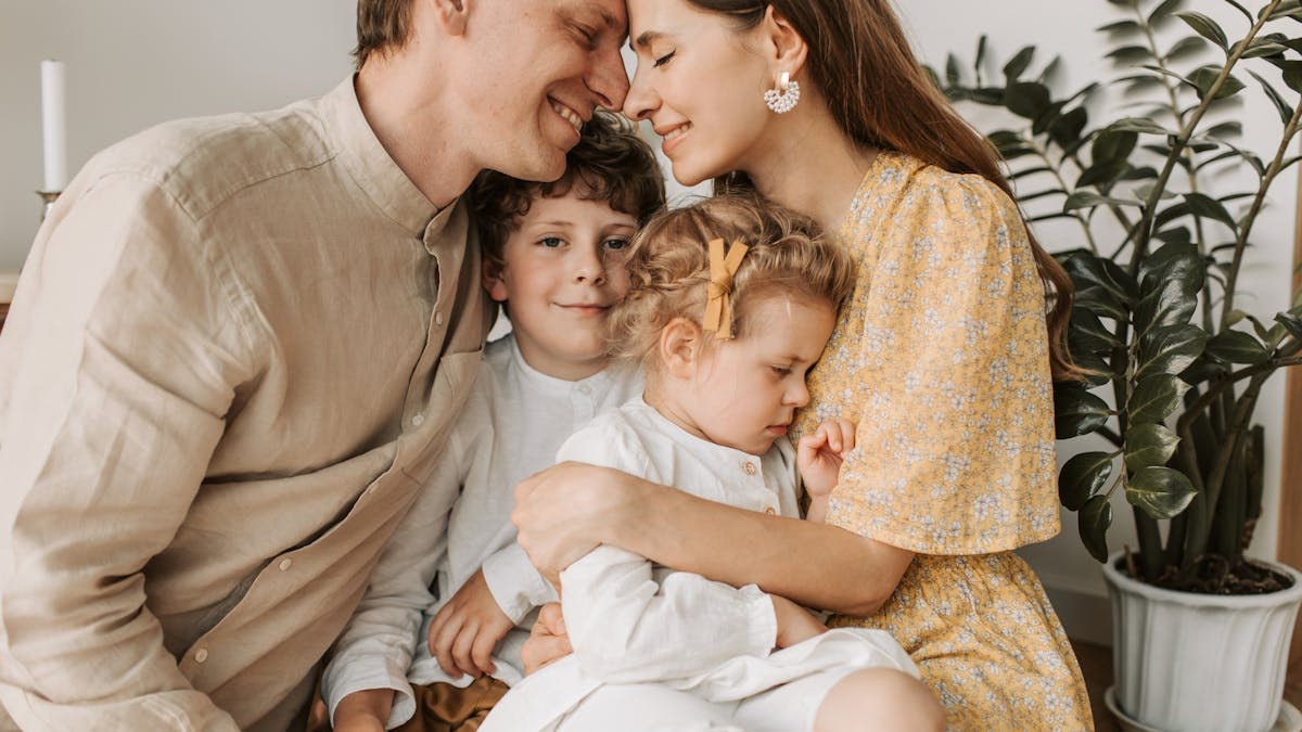 A loving family of four shares a tender moment in a cozy indoor setting, embracing and smiling.