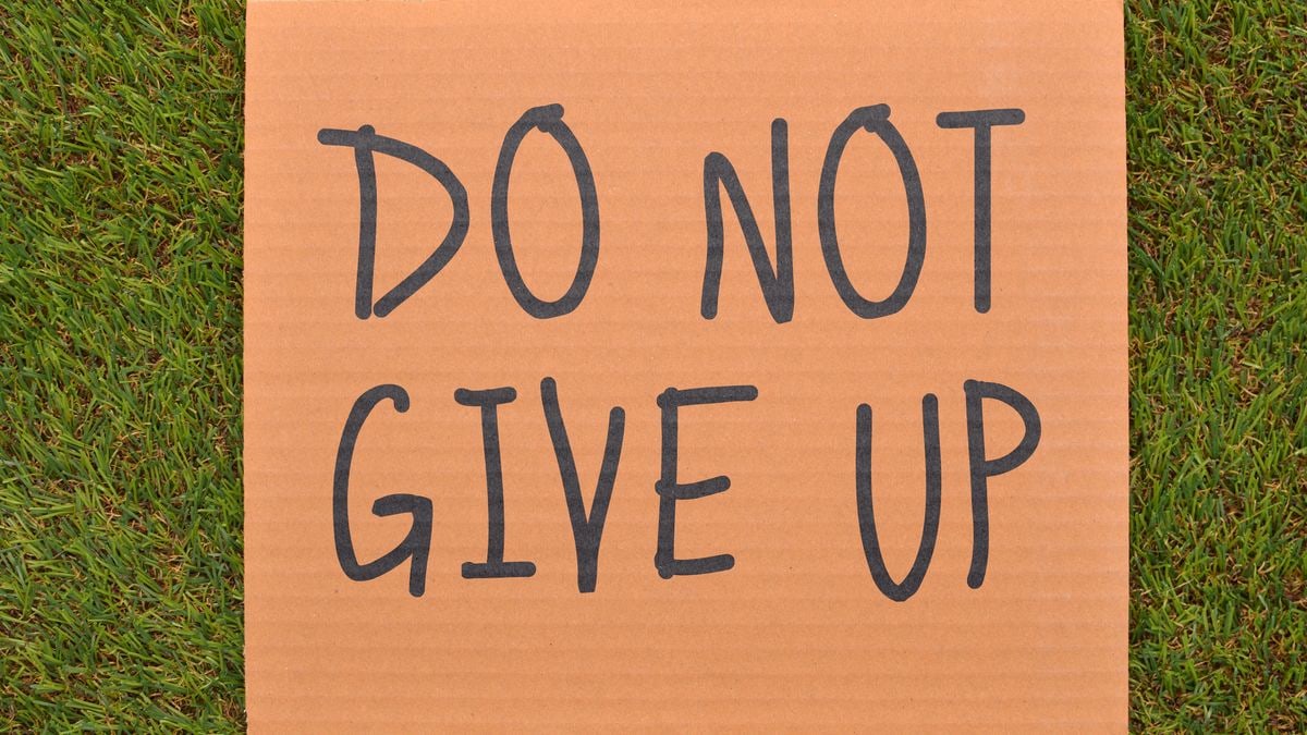 Cardboard sign reading 'Do Not Give Up' placed on green turf, symbolizing perseverance.